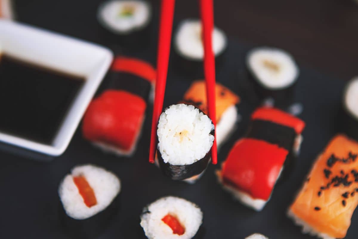 Sushi rolky a nigiri na tmavom tanieri s paličkami, teplé svetlo zboku.